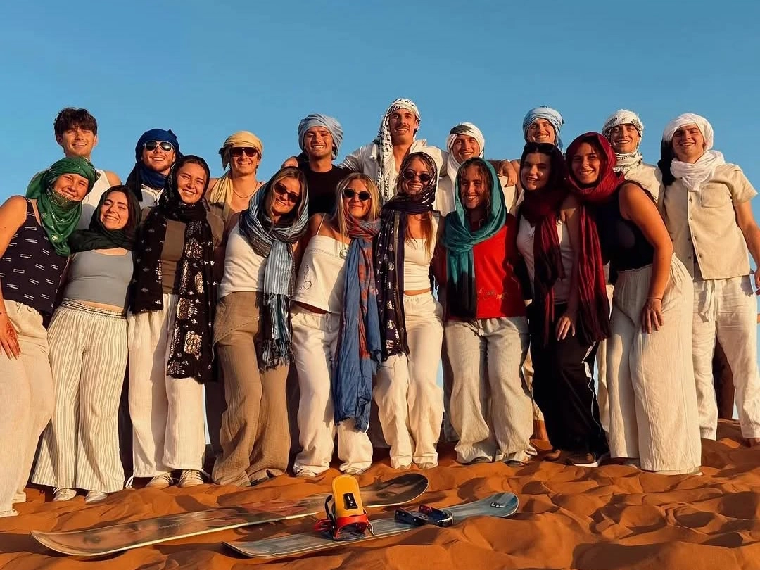 3 days desert tour from Marrakech — happy group of travelers with Berber scarves and sandboards on the Erg Chebbi dunes, Merzouga Sahara Morocco