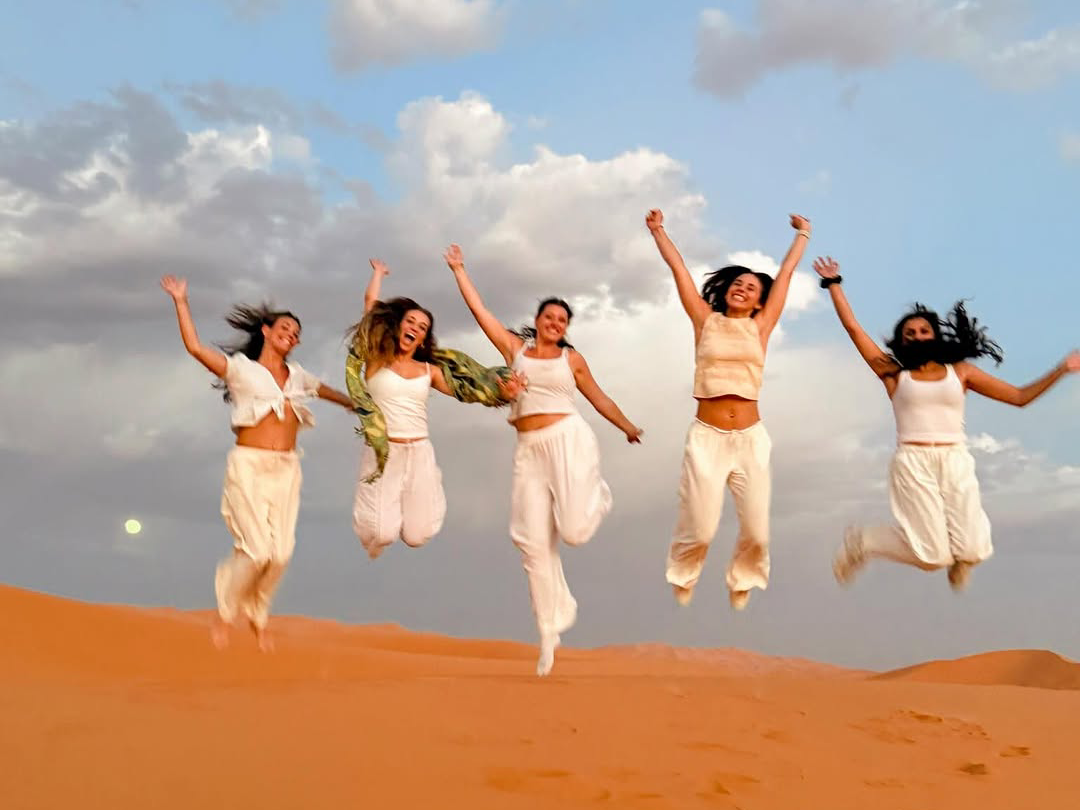 4 days desert tour from Marrakech — group of five women jumping with joy on Erg Chebbi dunes Merzouga Sahara Desert Morocco