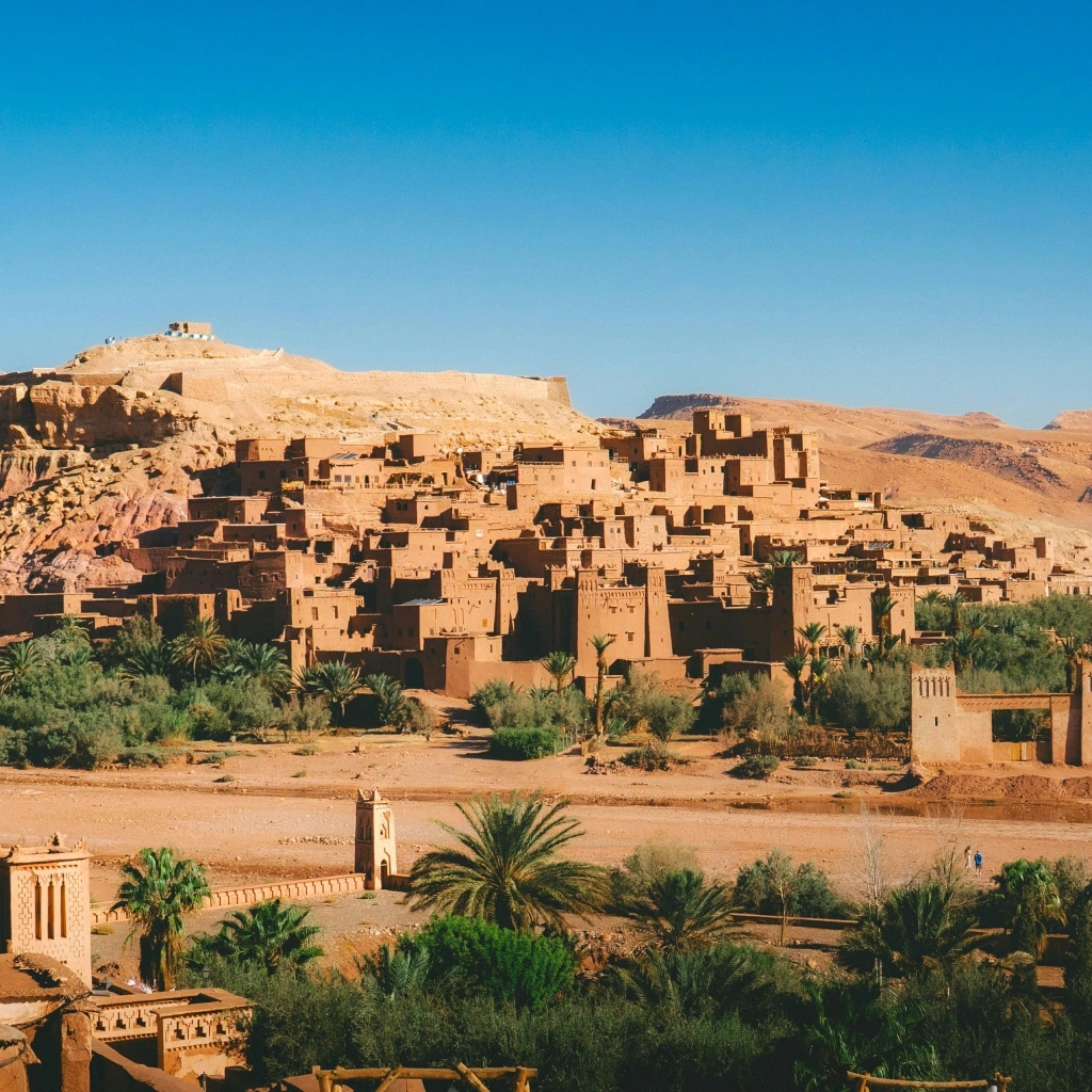 4 days desert tour from Marrakech — Aït Benhaddou UNESCO World Heritage ksar aerial view on hillside with palm trees and river Morocco