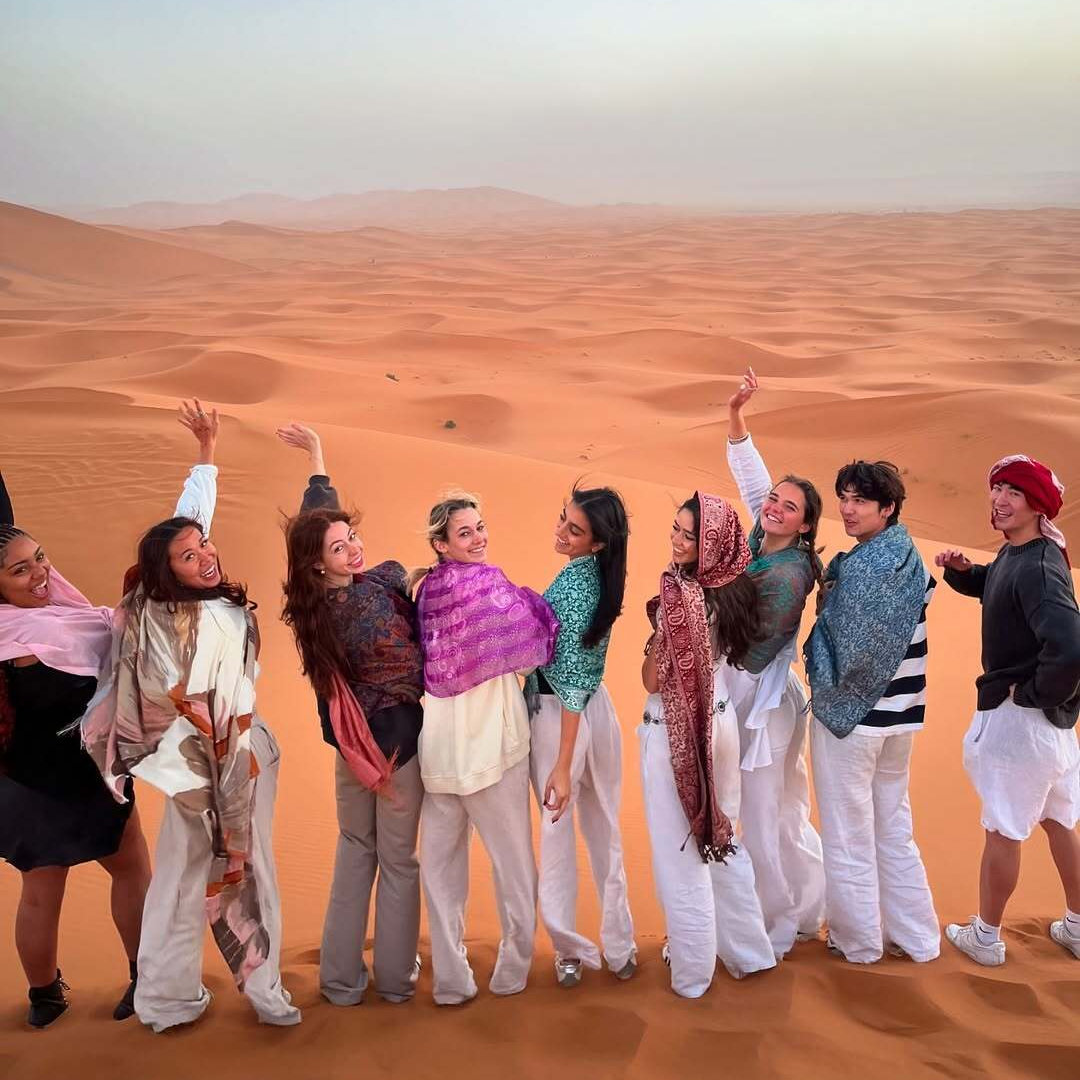 4 days desert tour from Marrakech — group of travelers celebrating on Erg Chebbi dunes wearing Berber scarves Merzouga Sahara Desert Morocco
