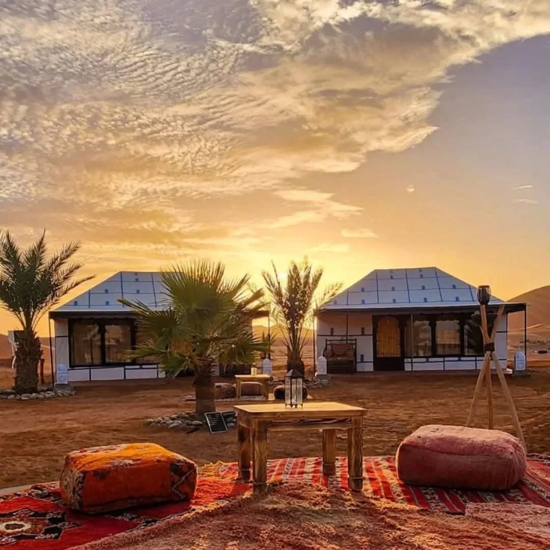 4 days desert tour from Marrakech — luxury Berber desert camp at sunset with Moroccan rugs palm trees and golden sky Merzouga Sahara Morocco