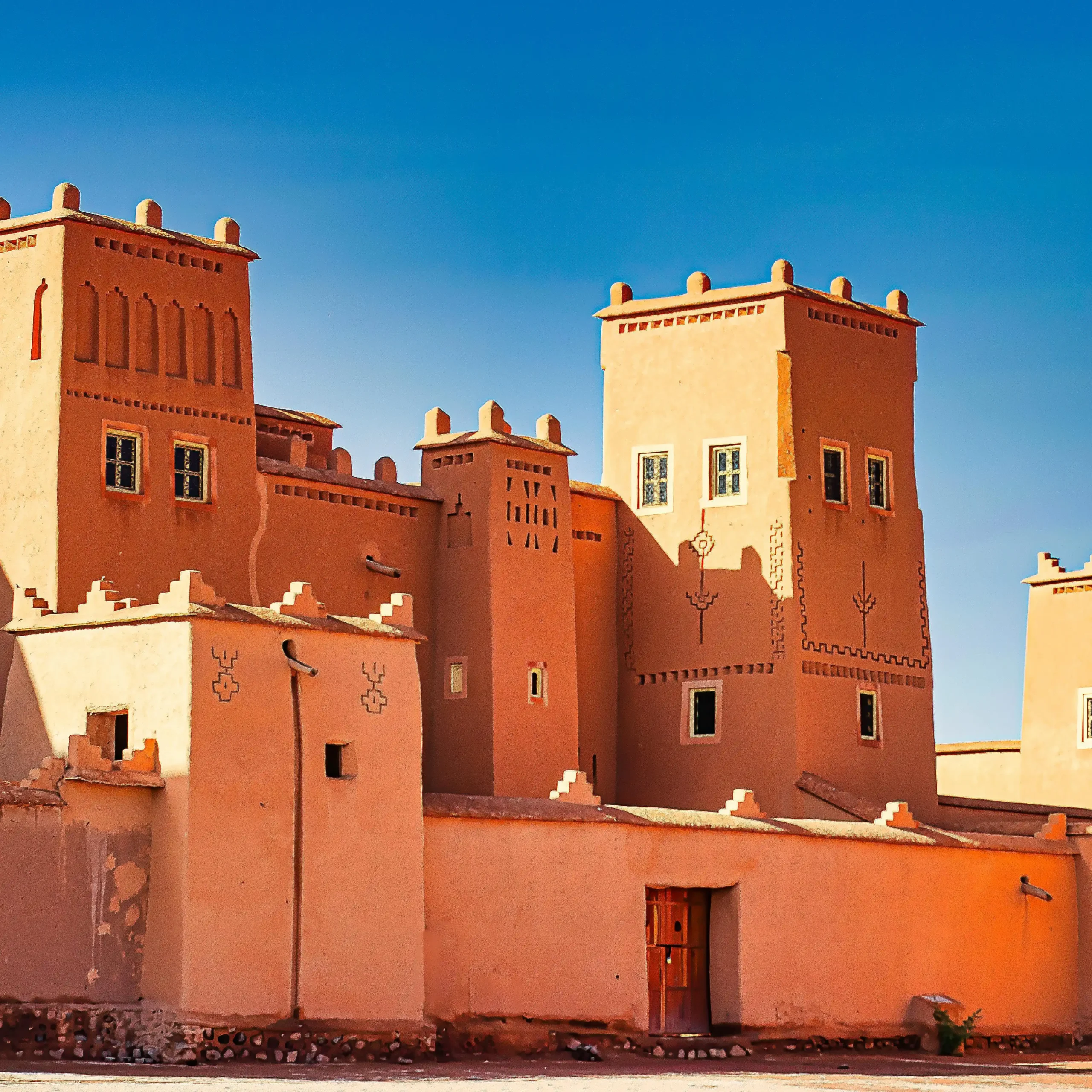 4 days desert tour from Marrakech — Taourirt Kasbah Ouarzazate tall red clay towers with geometric Berber carvings blue sky Morocco Day 1