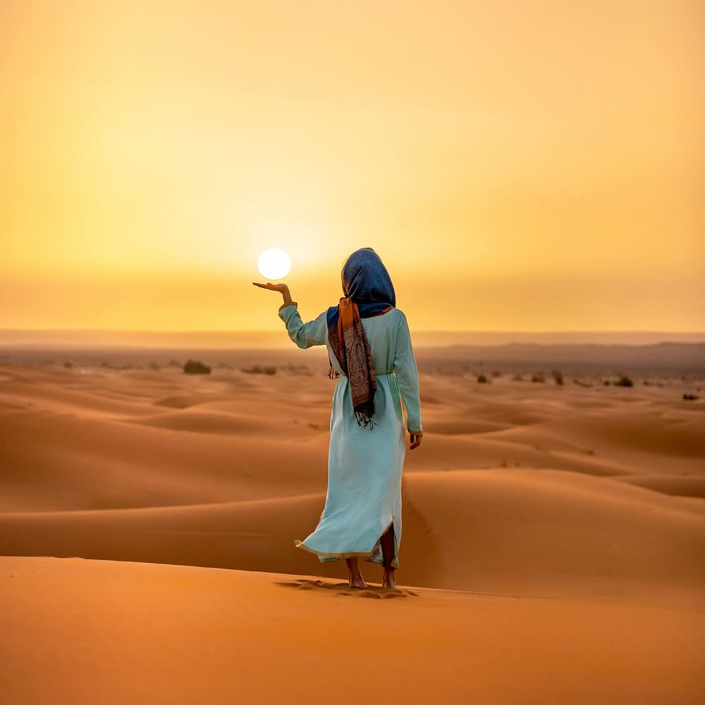4 days desert tour from Marrakech — woman in blue robe standing on Erg Chebbi dune at golden sunset Merzouga Sahara Desert Morocco