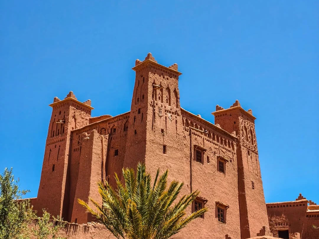 Towering mud-brick towers of Ait Benhaddou UNESCO World Heritage kasbah against a deep blue sky, a stop on the 3-day Marrakech to Fes desert tour