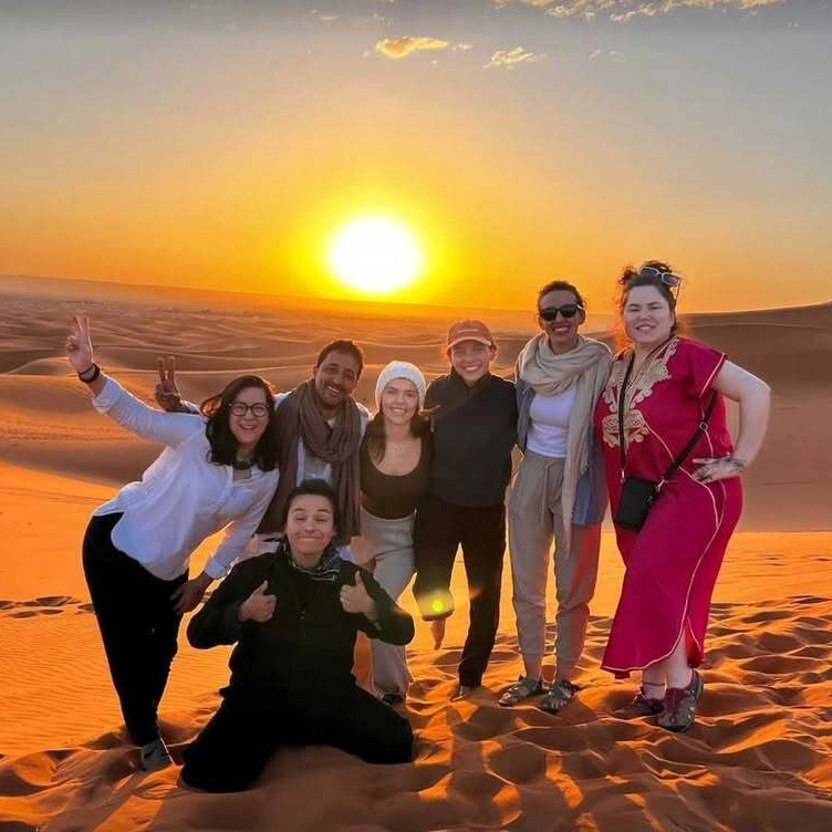 3 days desert tour from Marrakech — group of happy travelers celebrating sunset on the Erg Chebbi dunes Merzouga Sahara Desert Morocco