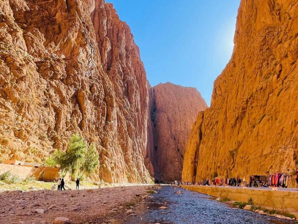 Towering red rock walls of Todra Gorge with a shallow river on the canyon floor in the Atlas Mountains, a stop on the 3-day Marrakech to Fes desert tour