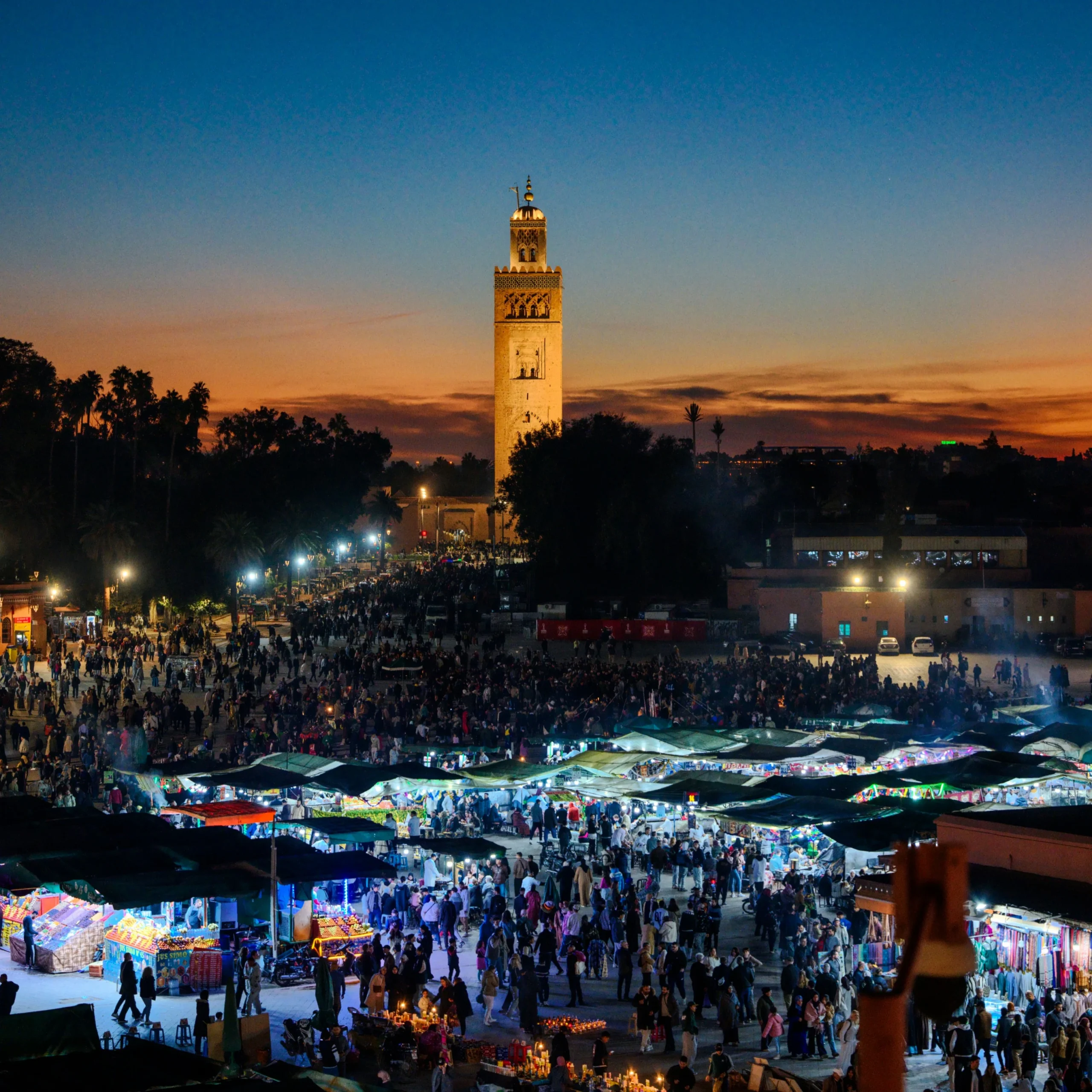 Morocco tours from Marrakech — Jemaa el-Fna square at night with glowing food stalls and Koutoubia mosque Marrakech Morocco